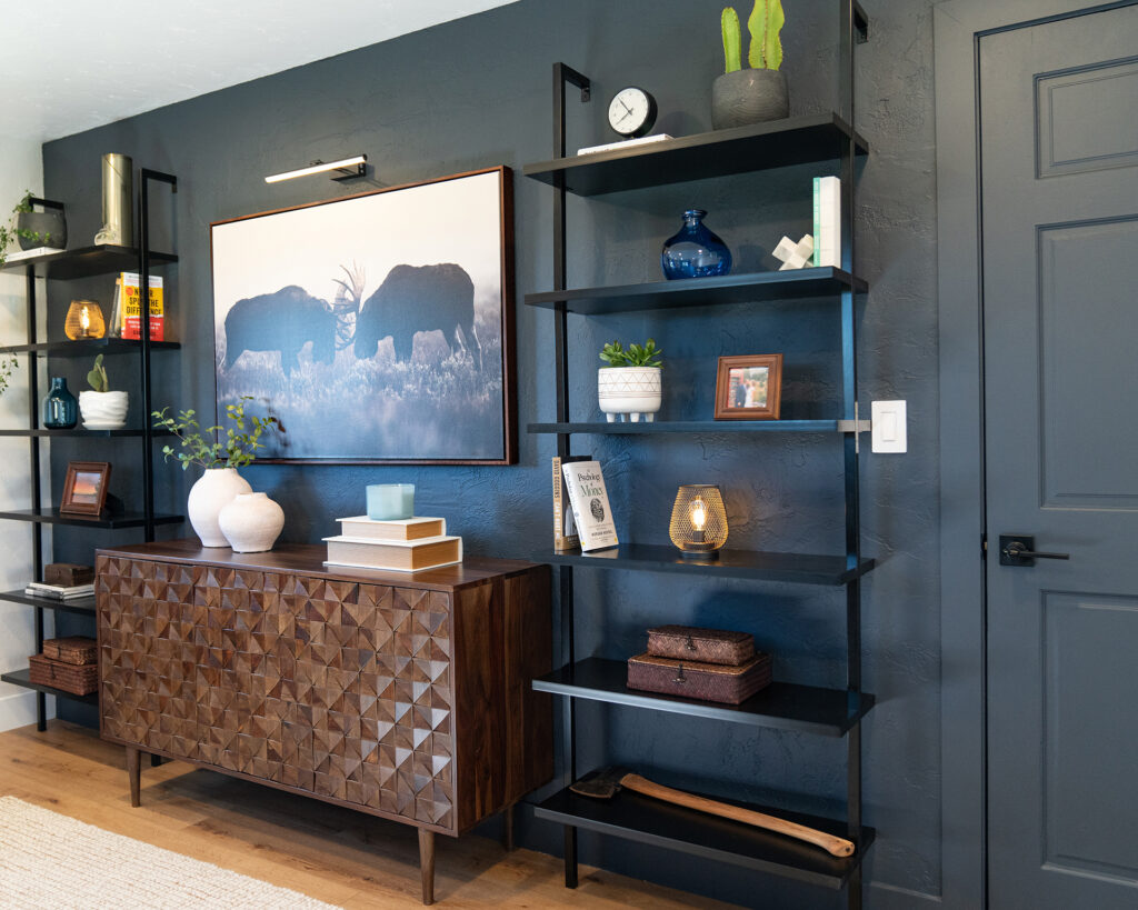Moody blue black accent wall in mens office with black ladder shelves and walnut sideboard