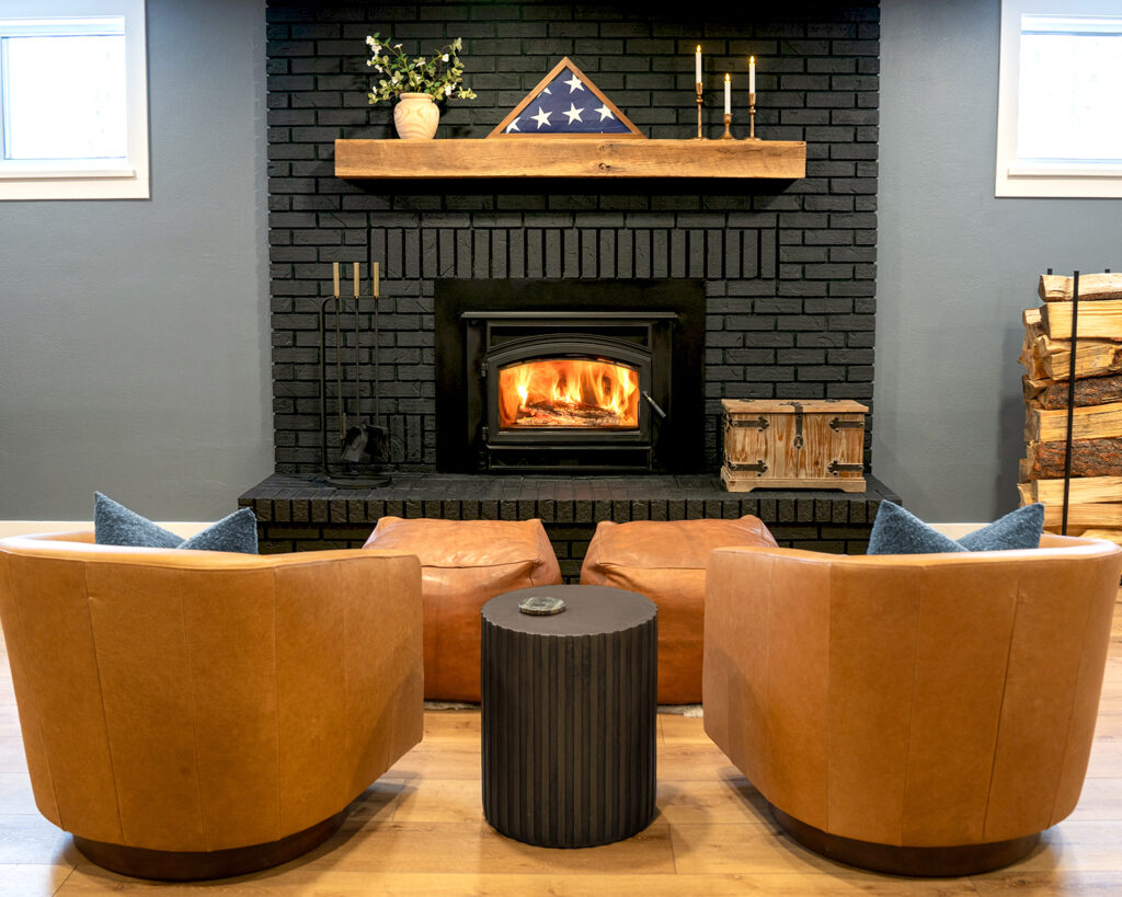 Painted black brick fireplace with wood burning stove and reclaimed beam mantle, blue grey walls and leather swivel chairs