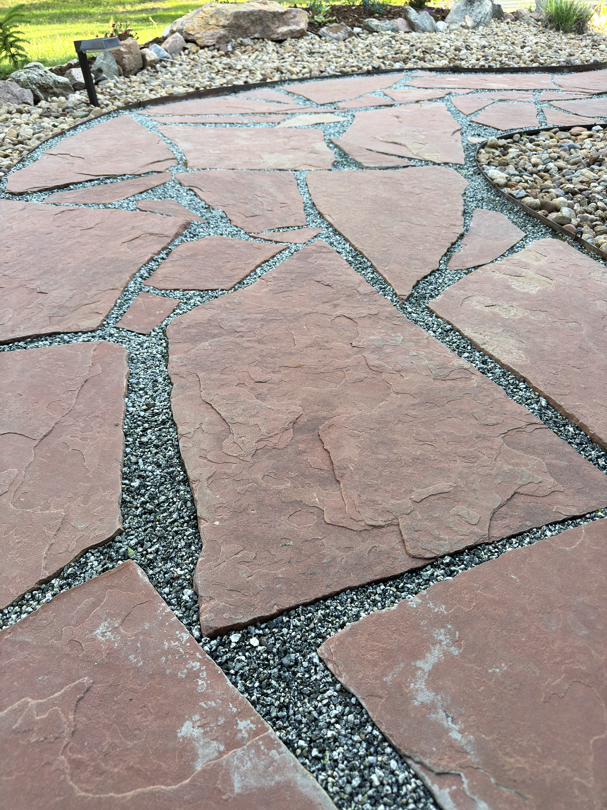 Closeup of red fagstone pathway with grey crushed pea gravel in between cracks glued with rock and gravel glue