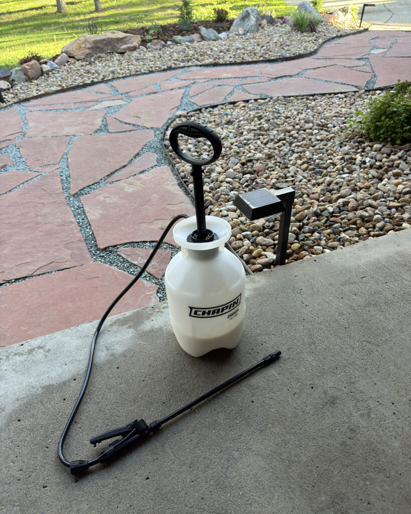 garden pump sprayer with rock glue mixture ready to apply on pea gravel pathway